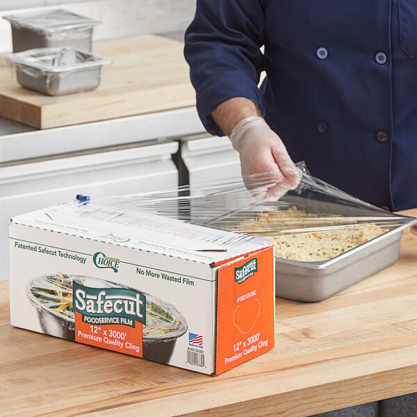 A person wearing gloves uses Choice Safecut Premium Foodservice Film to wrap food on a counter.