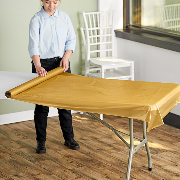 A woman rolling out a metallic gold plastic tablecloth over a table.