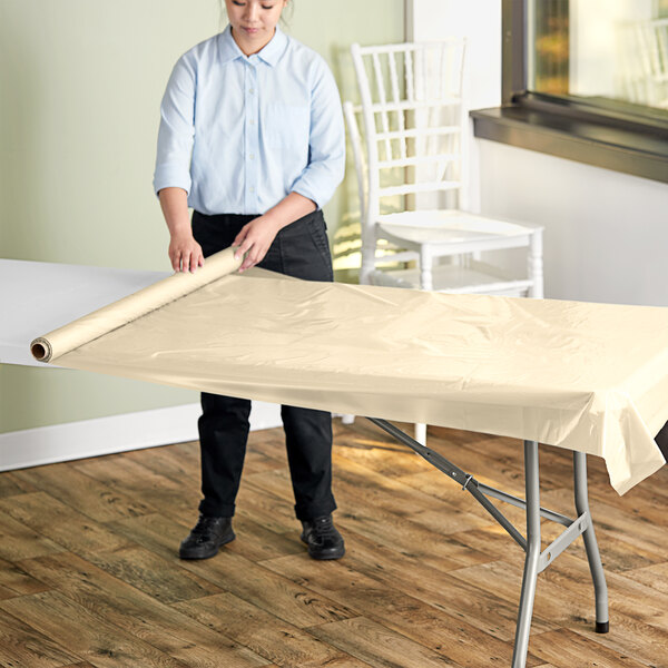 A woman rolling out a plastic table cover from a roll.