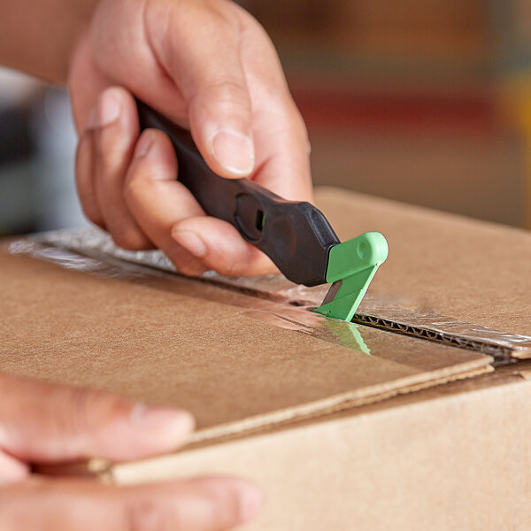 A hand holding a Klever Kutter EcoXChange box cutter and cutting a cardboard box.