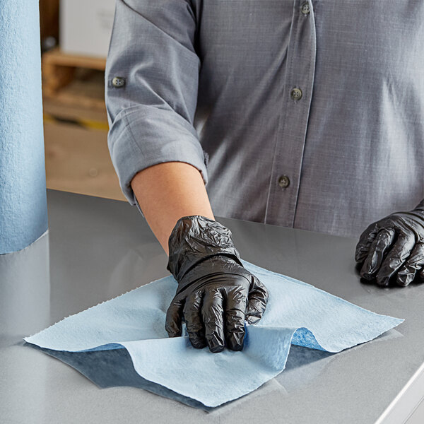 A person wearing black gloves cleaning a table with a Scott Shop Towel.