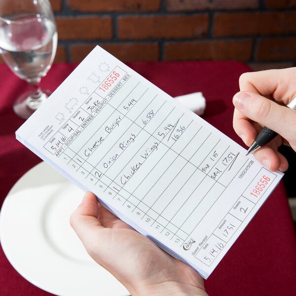 A hand holding a pen writing on a green and white Choice guest check.