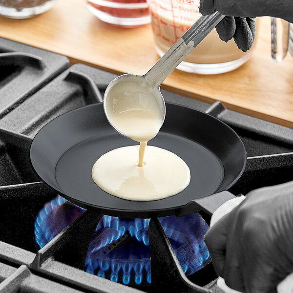 A person pouring white liquid onto a Matfer Bourgeat carbon steel crepe pan.