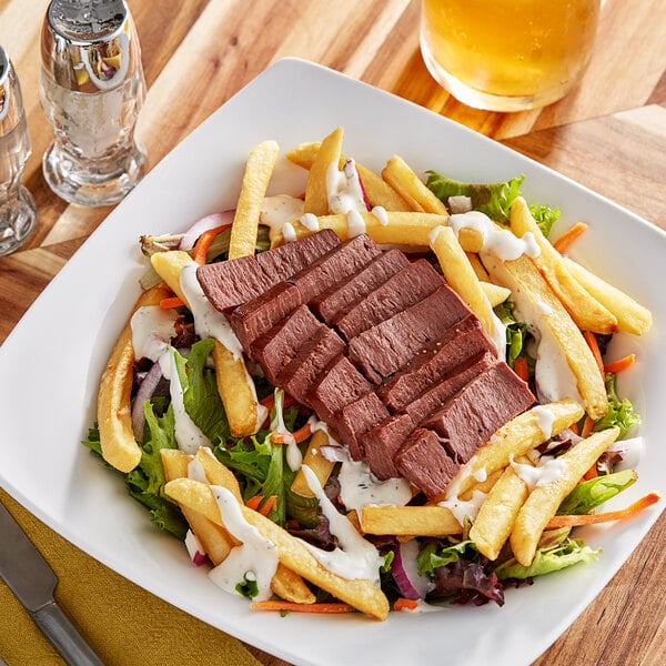 A plate with Eat Meati plant-based steak and fries on a table with a salad.