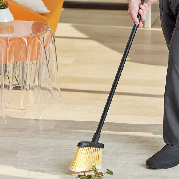 A person using a Carlisle yellow flagged angled lobby broom to sweep the floor.