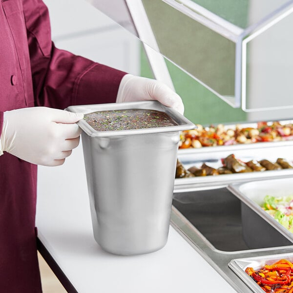 A hand holding a Vollrath stainless steel container of food.