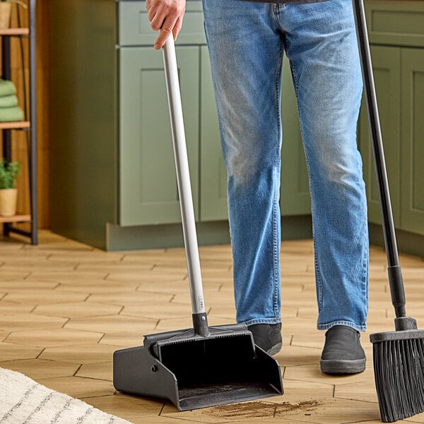 A man using a Carlisle black upright dustpan with a metal pole.