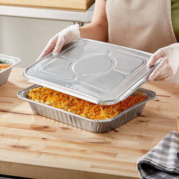 A person holding a Choice heavy-duty foil steam table pan filled with food.