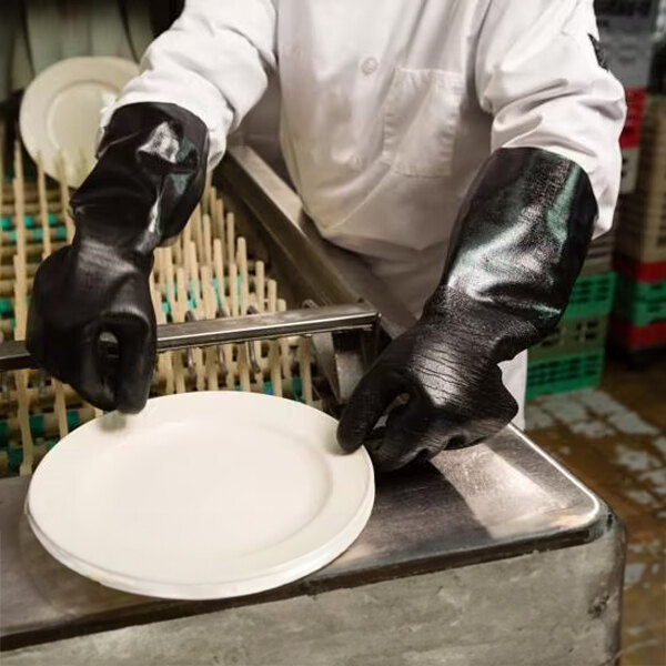 A pair of black neoprene dishwashing gloves with jersey lining being worn by a person handling dishes.