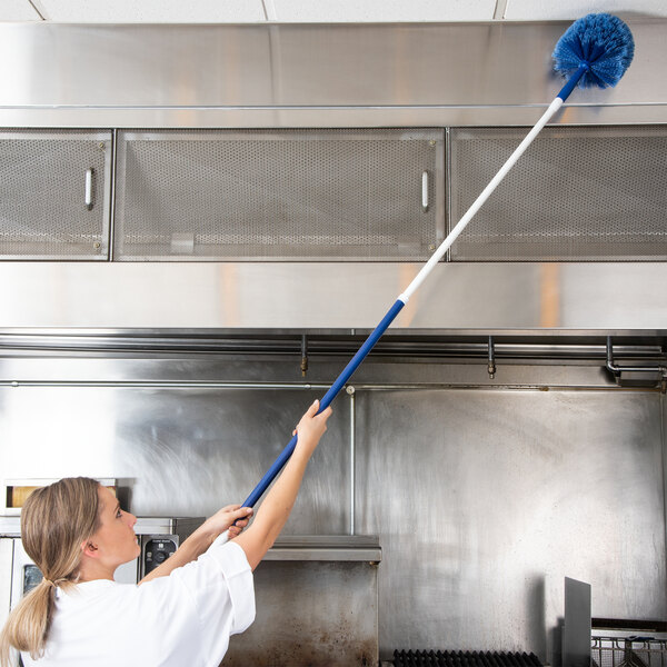 A person using a Carlisle 34" - 59" Flo-Pac telescopic handle with a blue duster to clean a high surface in a commercial kitchen.