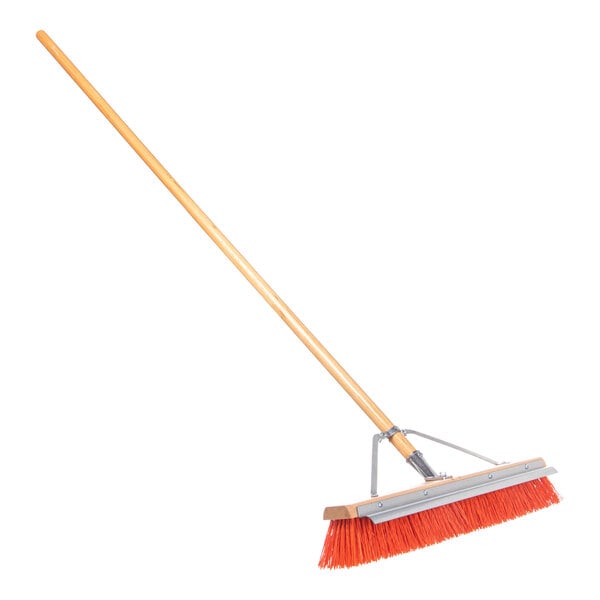 A Carlisle commercial hardwood push broom with a long orange wooden handle.