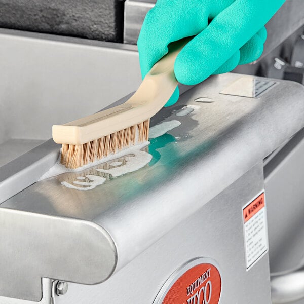 A person using a Carlisle Sparta narrow detail brush with tan bristles to clean a machine.