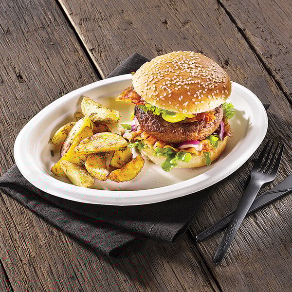 An oval-shaped compostable sugarcane plate with a burger and seasoned potato wedges.
