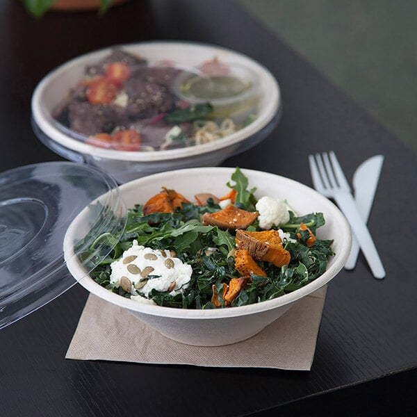 A compostable 32 oz. round noodle bowl made from sugarcane, shown with a clear lid and filled with salad.