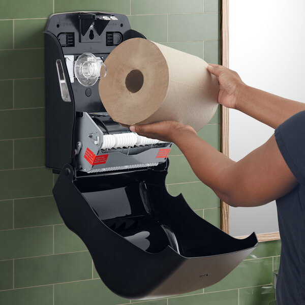 A woman using a San Jamar black mechanical hands free towel dispenser to dry her hands.