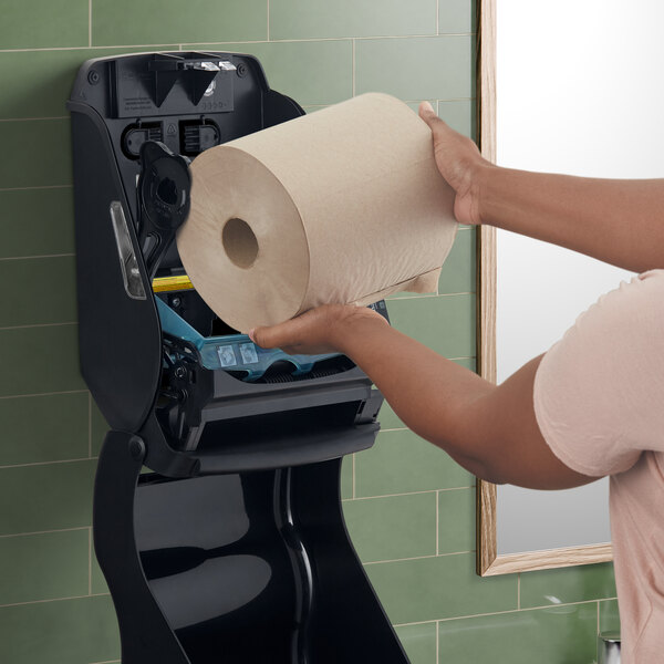A woman's hand using a San Jamar Tear-N-Dry black paper towel dispenser.