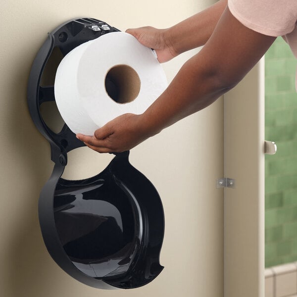 A hand holding a black roll of San Jamar EcoLogic jumbo toilet paper.