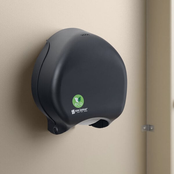 A black San Jamar single roll jumbo toilet paper dispenser mounted on a wall.