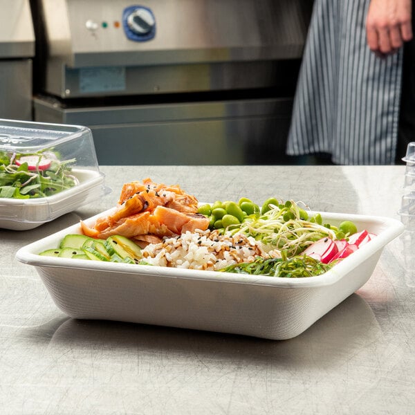 A white, square, compostable sugarcane container filled with assorted fresh food items.