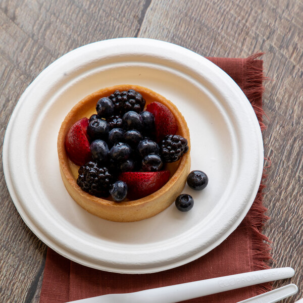 A small round compostable sugarcane plate holding a fruit tart with berries and strawberries.