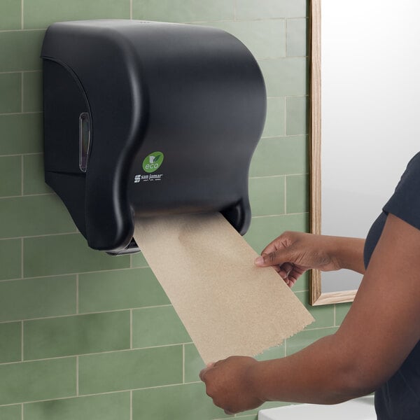 A woman using a black San Jamar Tear-N-Dry paper towel dispenser.