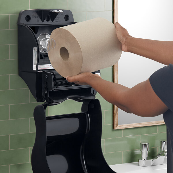 A woman using a San Jamar Tear-N-Dry black roll towel dispenser to get a paper towel.