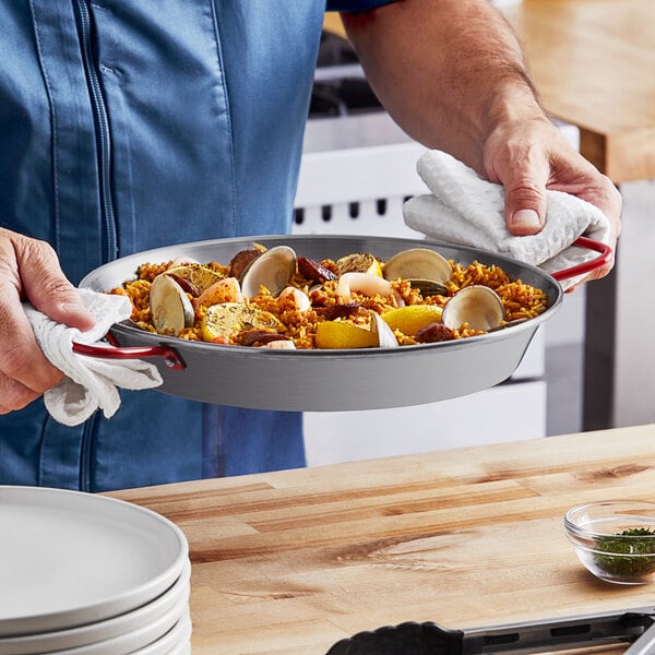 A person holding a Matfer Bourgeat paella pan of seafood and rice.