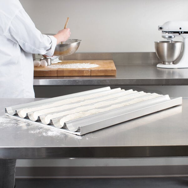 A person in a white coat mixing dough in a metal pan.