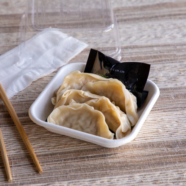 A small square compostable sugarcane container holding dumplings and a sauce packet.