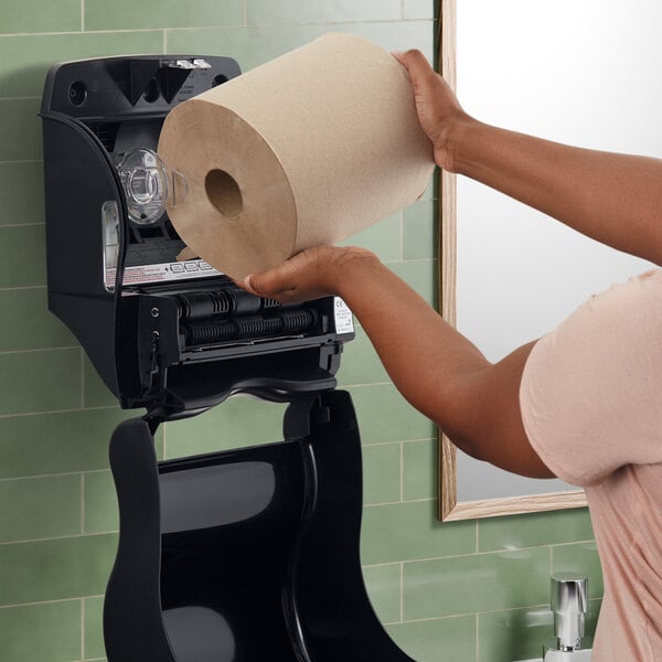 A woman using a San Jamar Smart Essence electronic roll towel dispenser in a corporate office cafeteria.