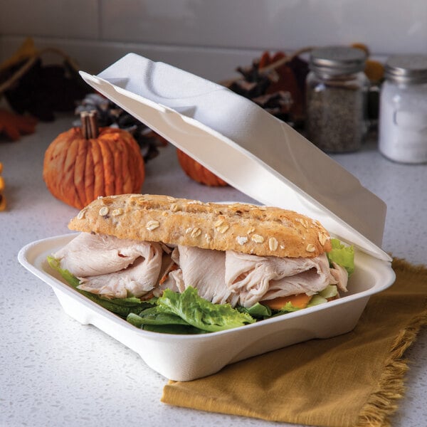 A compostable sugarcane clamshell container holding a sandwich with lettuce and sliced meat.