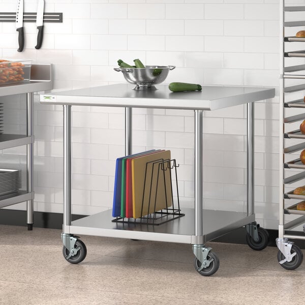 A Regency stainless steel work table with casters and a shelf holding different colored cutting boards.