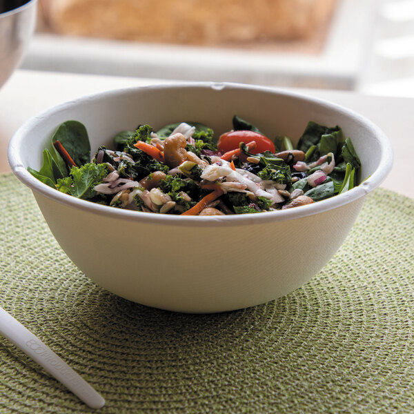 A large white compostable sugarcane bowl filled with salad, placed on a green woven placemat.