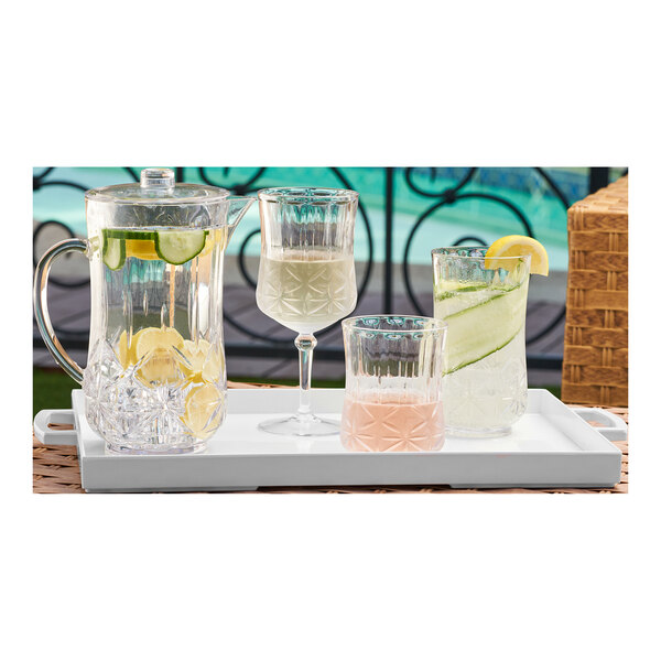 A tray with Sophistiplate clear plastic wine glasses and a pitcher of water on a white surface.