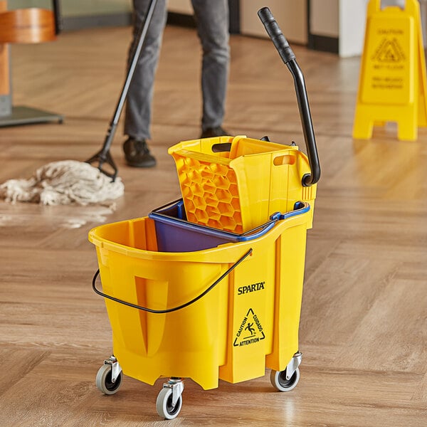 A man using a Carlisle yellow mop bucket with a wringer to clean a wood floor.