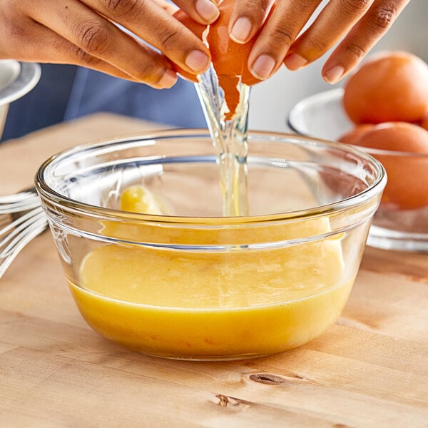 A person breaking an egg into a glass bowl of eggs.