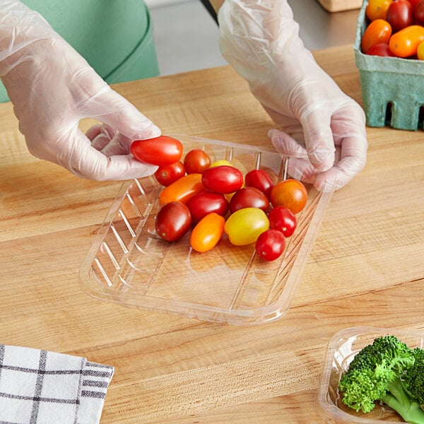 A hand in a glove holding a plastic container of cherry tomatoes.