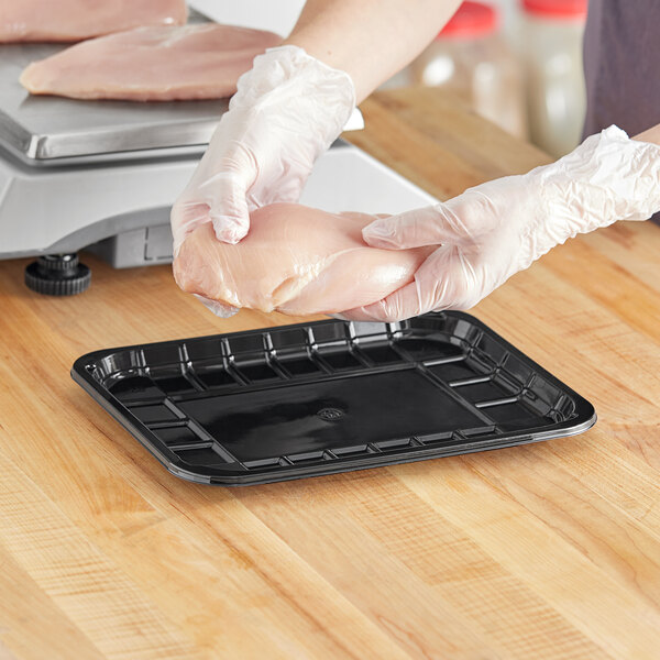 A person in gloves holding a black CKF PET plastic meat tray with a piece of chicken.