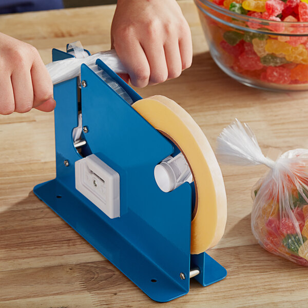 A hand using Lavex clear poly bag sealer tape to seal a plastic bag of gummy candies.