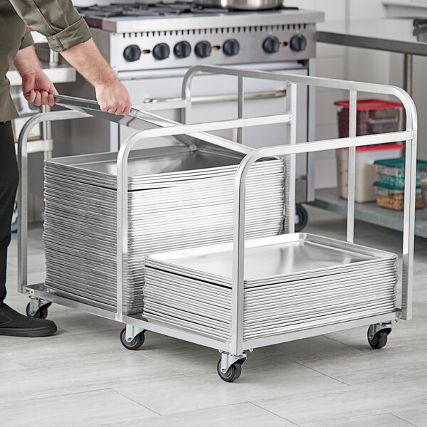 A person pushing a Regency aluminum double bun pan truck with a large stack of trays.