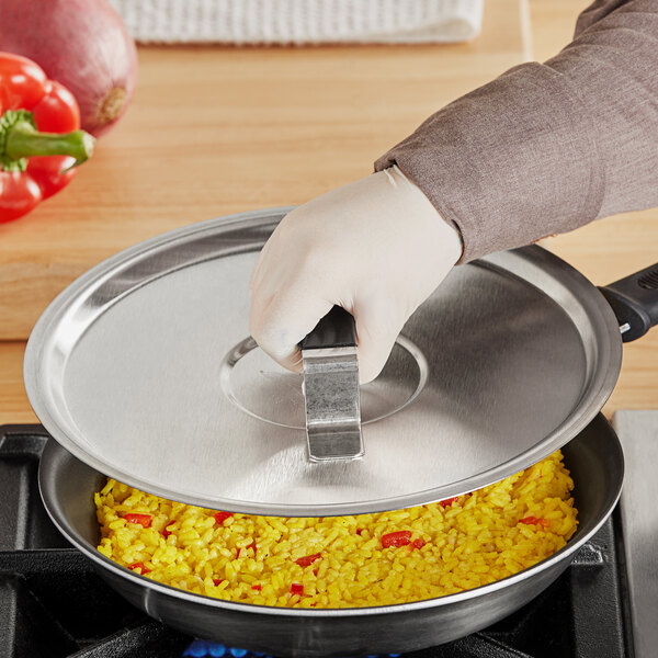 A person wearing gloves holding a Vollrath Tribute pan cover over a pan of rice