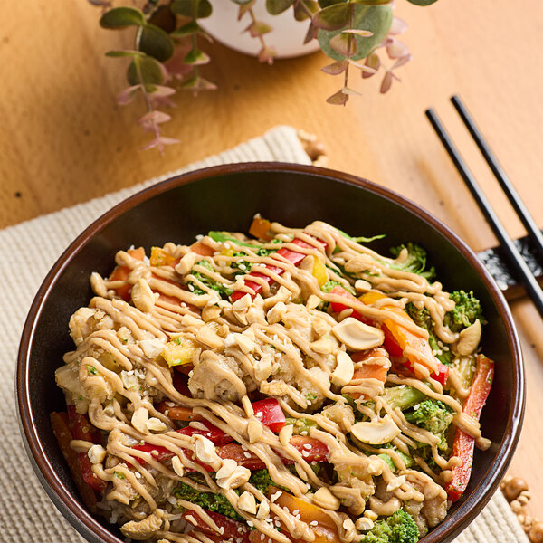 A bowl of broccoli and noodles with sauce and peanuts.
