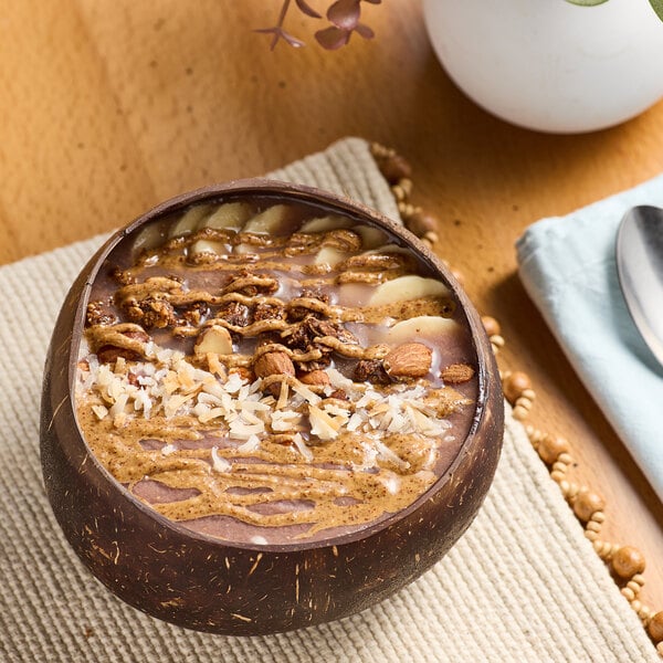 A bowl of smoothie with nuts and almond butter on a table in a juice bar.