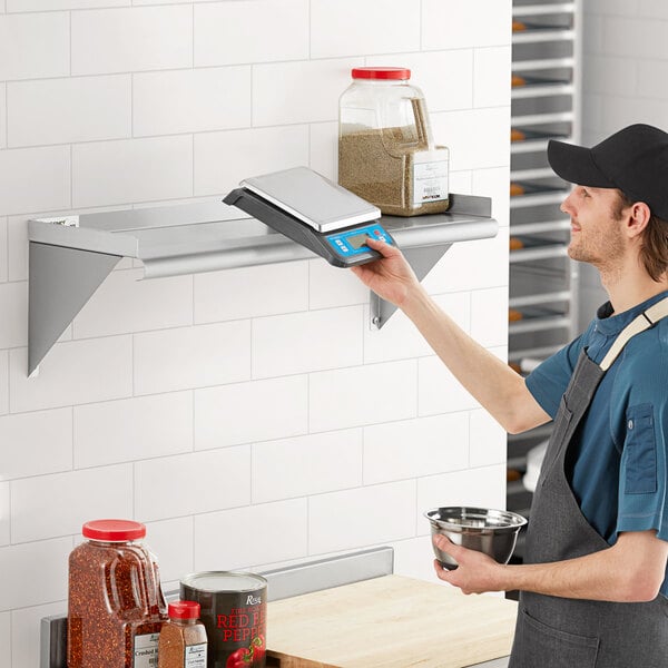 A man in an apron using a Regency stainless steel wall shelf in a professional kitchen.