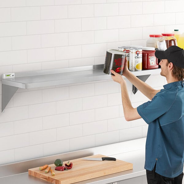 A man in a professional kitchen using a Regency stainless steel wall shelf to store food jars.