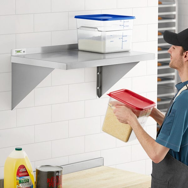 A man holding a plastic container of food on a Regency stainless steel wall shelf.