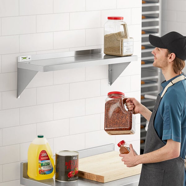 A man standing in front of a Regency stainless steel wall shelf with a plastic container of red flakes.