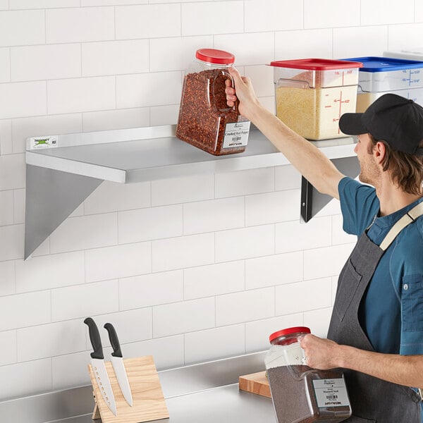 A man in a professional kitchen installing a Regency stainless steel wall shelf.