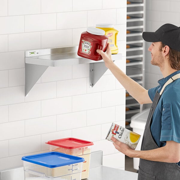 A man in a blue shirt installing a Regency stainless steel wall shelf.