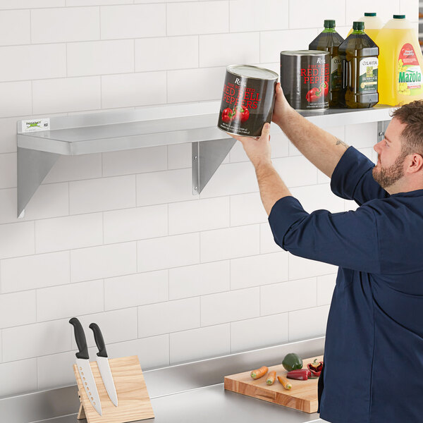 A man in a blue shirt holding a yellow jar on a Regency stainless steel wall shelf.